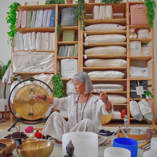 Mi Sun seated with her singing bowls, crystal bowls and gong, surrounded by the gallery's display shelves