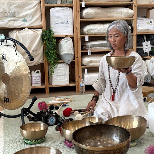Mi Sun lifting a brass singing bowl, with the gong set up beside her