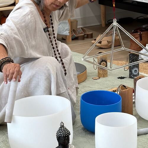 Crystal bowls and a copper pyramid arranged on the mat, with a guest resting on a mattress behind